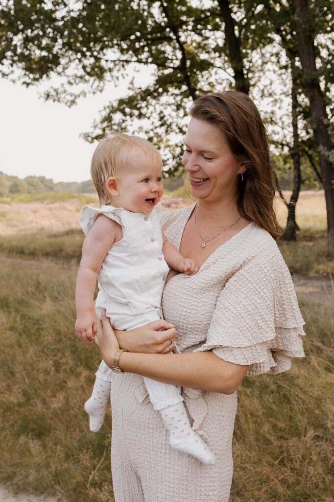 Mama houdt dochter vast en lacht naar haar tijdens familie fotoshoot