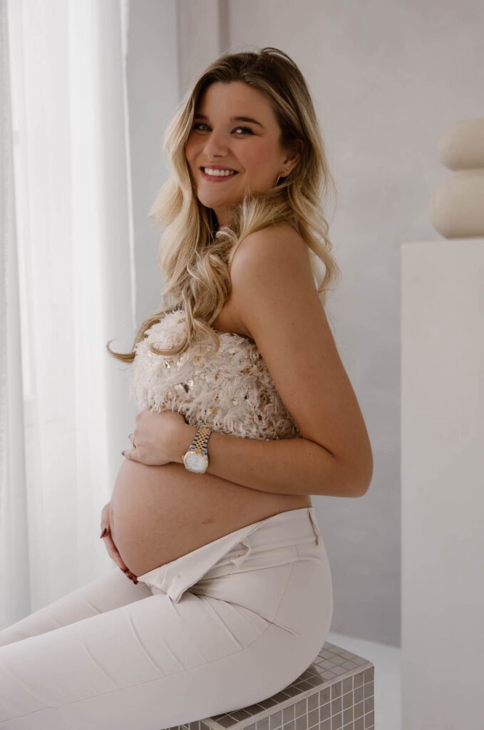 Zwangere vrouw in top met veren en pailletten en neutrale broek tijdens zwangerschapsshoot in Amsterdam bij Atelier Oost