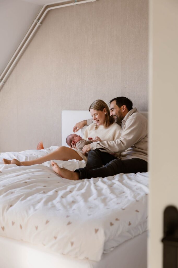 Ouders met pasgeboren baby op bed tijdens newbornshoot thuis