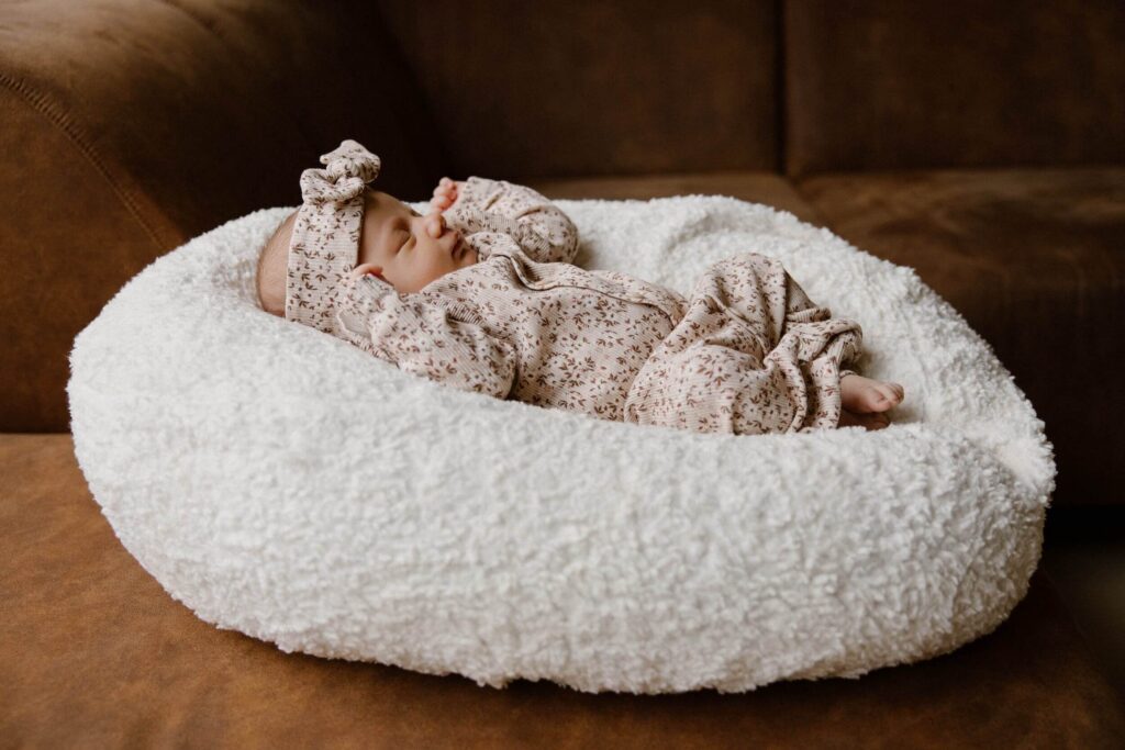 Pasgeboren meisje in romper en haarband met bloemen slaapt op teddy kussen tijdens newbornshoot