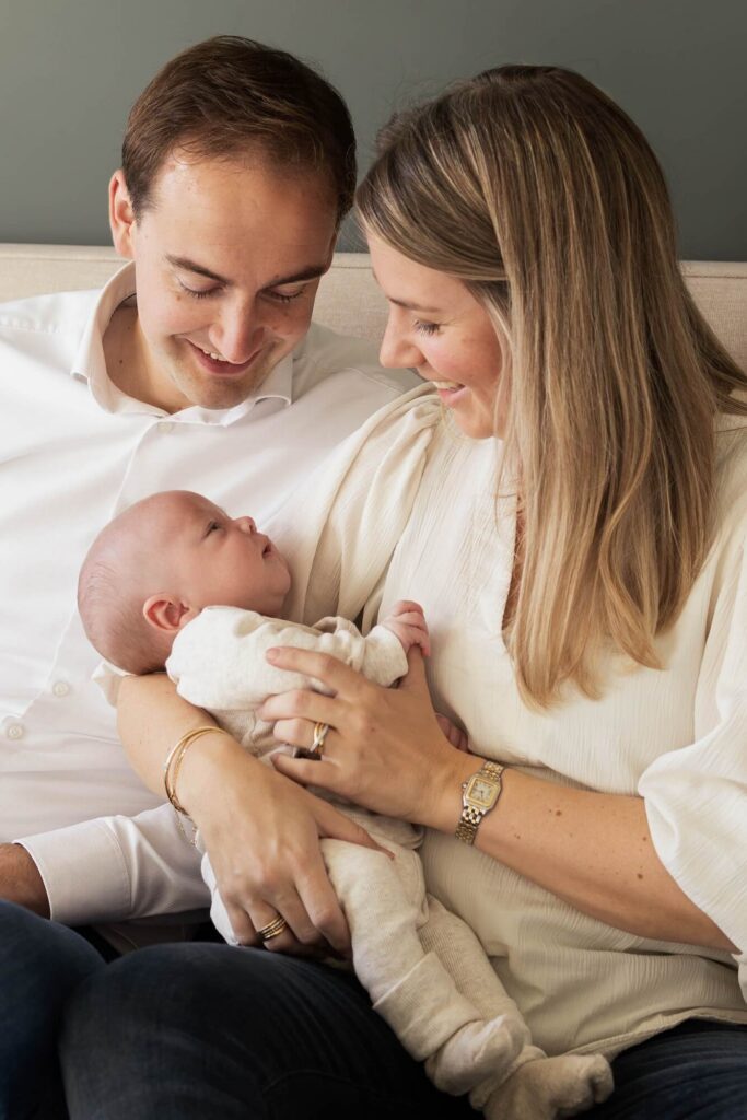 Baby ligt in de armen van mama, mama en papa kijken baby lachend aan