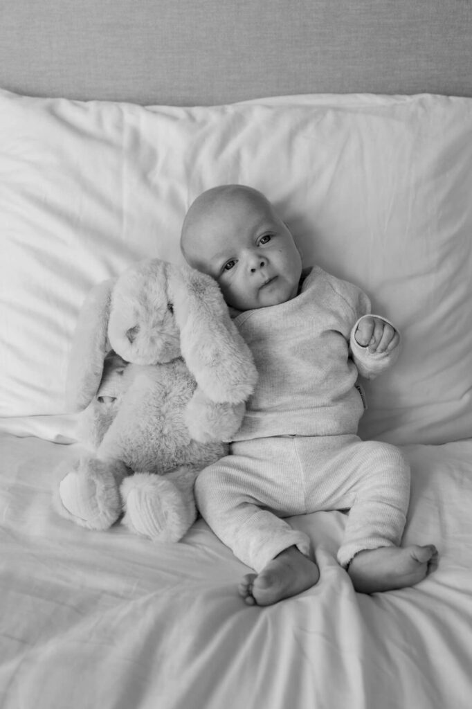 Baby ligt tegen kussen op bed met konijn knuffel