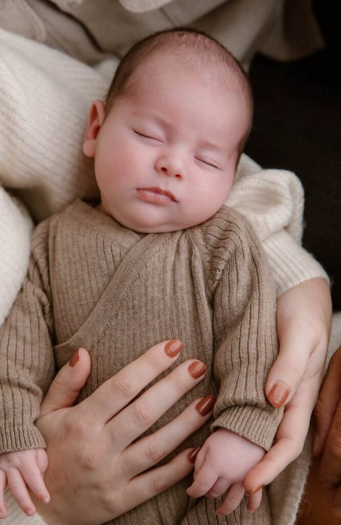 Pasgeboren baby in bruin gebreide romper slaapt in de armen van mama