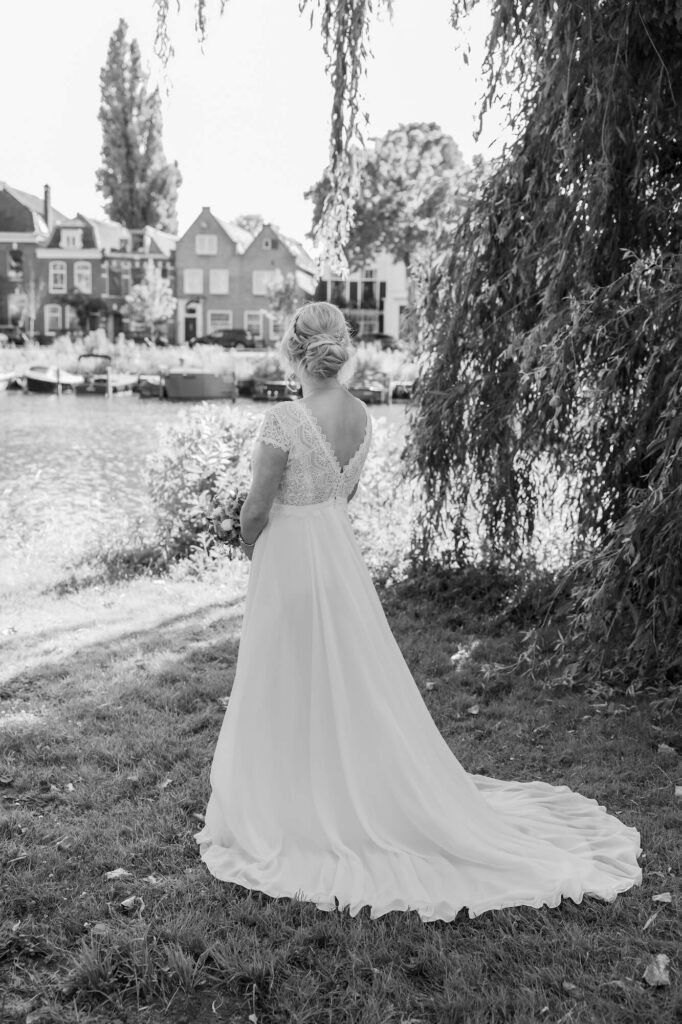 Zwart-wit foto van bruid in witte jurk kijkend over gracht in Weesp