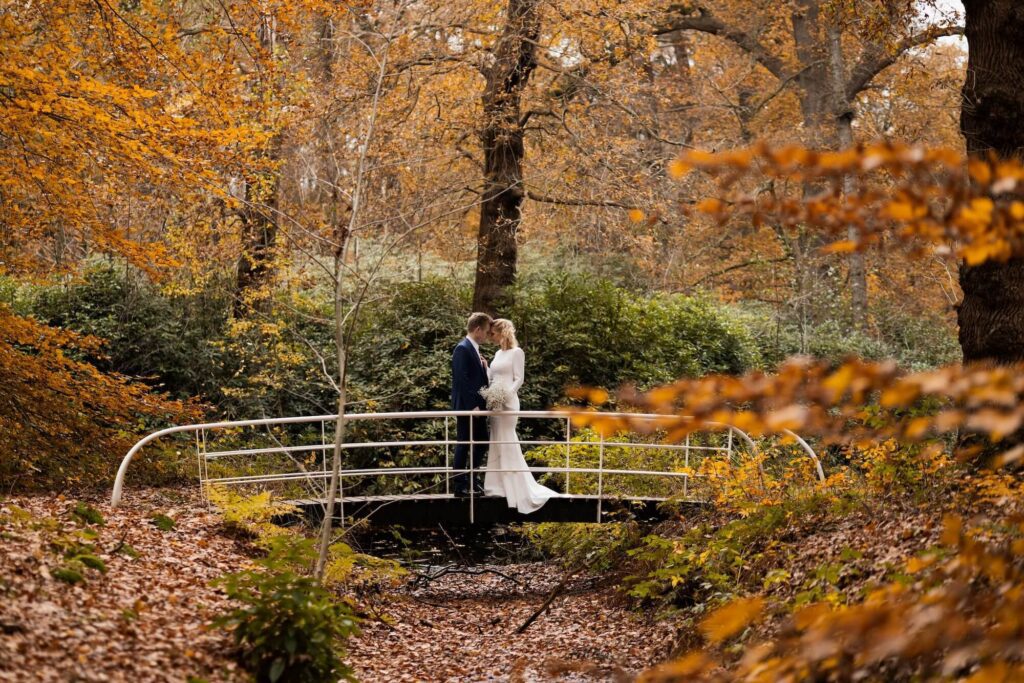 Bruidspaar op een witte brug in het bos van Weesp met warme herfstkleuren