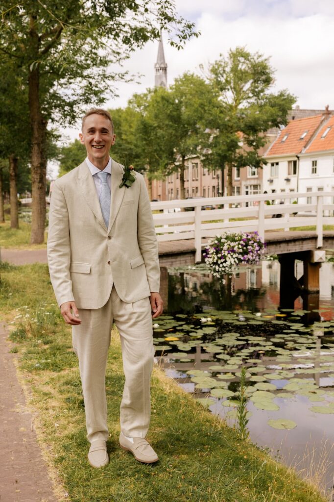Bruidegom in beige pak wandelt naast gracht van Weesp