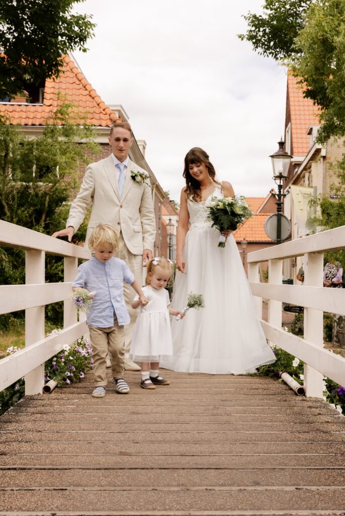 Bruidspaar wandelt met zoon en dochter op witte brug over de gracht in Weesp