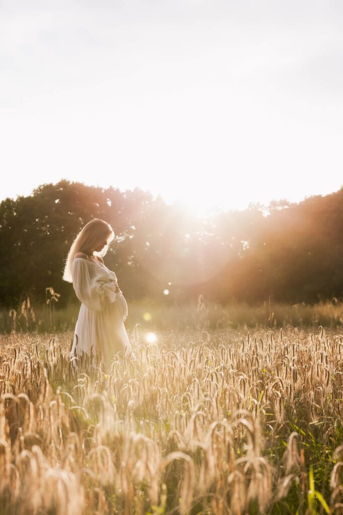 Vrouw in witte lange jurk in graanveld tijdens golden hour zwangerschapsshoot