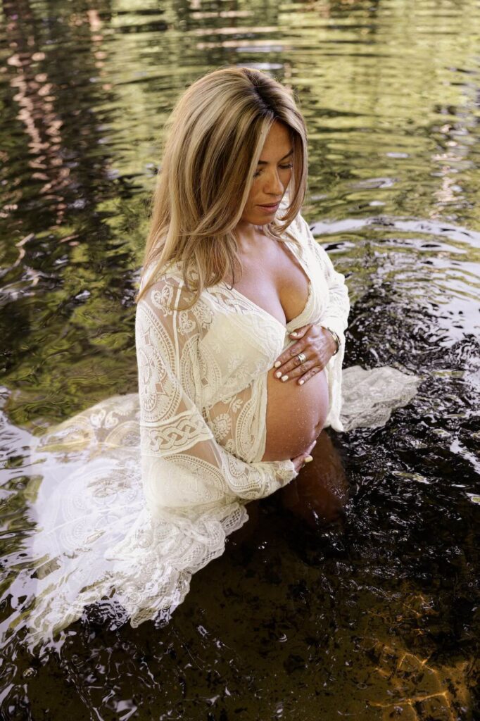 Vrouw in witte kanten kimono in het water tijdens zwangerschapsshoot